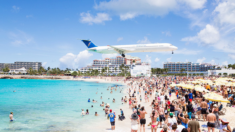 Antes de Irma: esta es la playa de Maho, en la islita de Saint Martin, célebre por hallarse a escasos metros de la pista de aterrizaje del Aeropuerto Internacional Princesa Juliana, lo que hace que los aviones, durante las maniobras de aterrizaje, la sobrevuelen apenas a unos 25 metros por encima de las personas que disfrutan del baño o descansan en la arena.