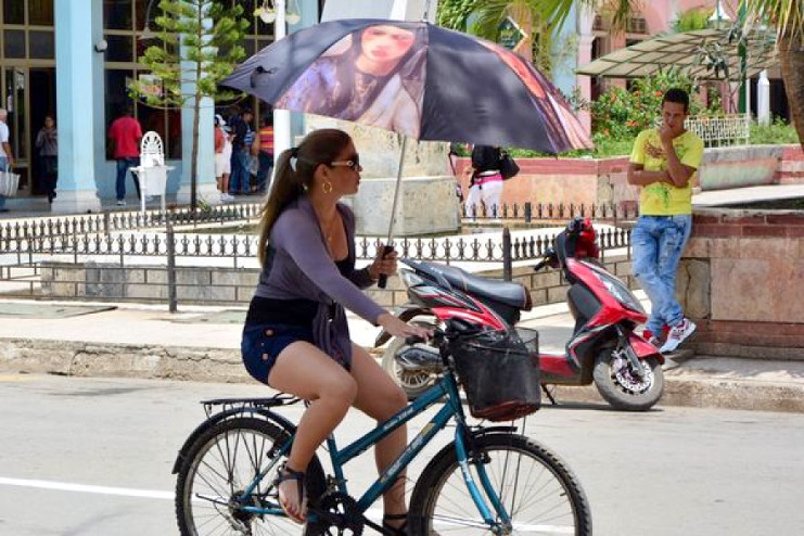 Mujer en bicicleta con sombrilla para protegerse del intenso sol del verano cubano. /Foto: Osvaldo Gutiérrez Gómez (ACN)