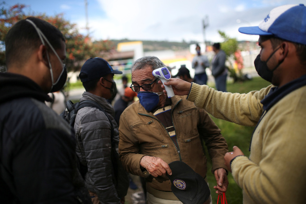 Migrante venezolano toma la temperatura de un hombre que ingresa a un campamento en Bogotá. 8 de junio de 2020. /Foto: Luisa Gonzalez (Reuters)