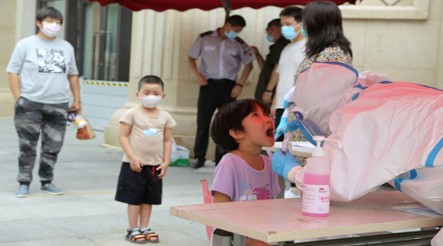 Trabajador sanitario con indumentaria protectora toma una muestra de saliva a un niño para hacer una prueba del coronavirus, el 27 de julio de 2020 en Dalian, al noreste de China. /Foto: AFP