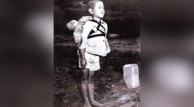 3.Un niño japonés de unos 10 años carga el cadáver de su pequeño hermano sobre su espalda en espera de su turno en el crematorio, Nagasaki, agosto de 1945. / Foto de Joseph Roger O’Donnell)